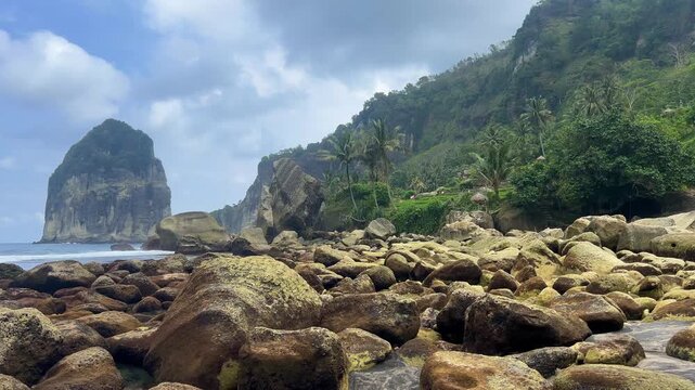 Pangasan Beach with high cliffs, Pasitan. Indian Ocean. View of a black sand beach and coral reef in East Java, Indonesia. Waves on the beach behind the picturesque cliffs. 4К