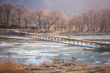Traditional Korean Brushwood Bridge (Seopdari) Crossing a Frozen Winter River in Yeongwol, South Korea (The Wisdom of Ancestors: A Handmade Rustic Bridge)
