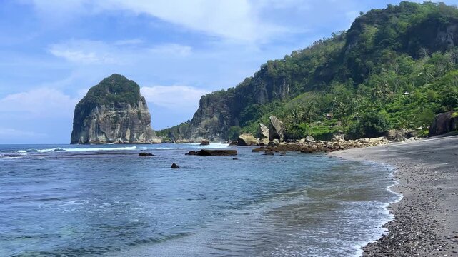 Pangasan Beach with high cliffs, Pasitan. Indian Ocean. View of a black sand beach and coral reef in East Java, Indonesia. Waves on the beach behind the picturesque cliffs. 4К