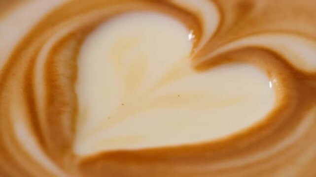 Macro slow motion of a heart-shaped chocolate melting on the surface of a steaming latte creating marbled patterns concept of sweet indulgence and romantic coffee break