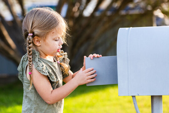 Girl opening mailbox in front yard checking for letters