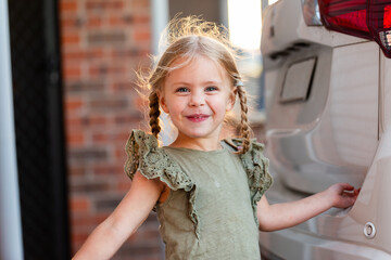 Little three year old child smiling and playing outdoors by car and brick home  