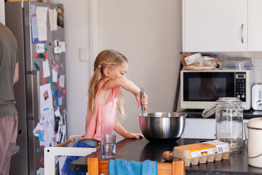 Little girl with whisk helping mix pancake mixture for breakfast in kitchen
