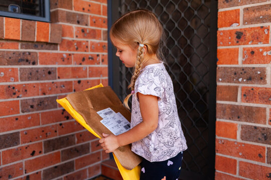 Little girl picking up parcel package delivery from doorstep of home in Australia