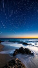 Long exposure of star trails over ocean, beach, and rocks