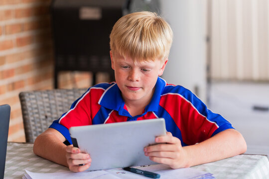 Boy in school uniform doing homework on tablet at table in backyard