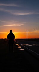 Fototapeta premium Solitary figure stands on the roadside against a vibrant sunset sky