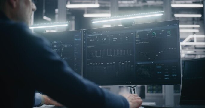 Technical Professional Sits at Well Organized Desk in Data Center, Using Dual Monitors to View Network Mapping and Performance Data. Concept of Big Data, Work Efficiency, and Organized Technical Work.