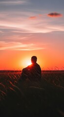 Obraz premium Solitary figure observes a brilliant orange sunset while seated amidst tall field grasses