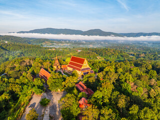 An aerial view of a serene temple nestled among lush green forested mountains, capturing the harmony between spiritual architecture and the surrounding natural landscape under a clear blue sky.