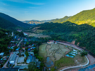 An expansive view of vibrant rice paddies arranged in terraces, surrounded by forested hills under a clear blue sky, symbolizing harmony between nature and agriculture. Winding River