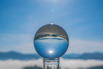 A crystal ball on an open road reflects a mist-covered mountain village, revealing a surreal persp Perspective of the Unknown Crystal Ball on a Misty Road ective of a journey into the unknown.