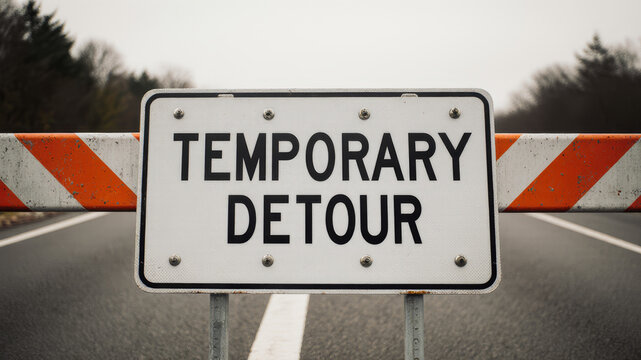 Temporary detour warning sign placed on striped barricade showing blocked route or redirected transport path