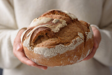 Close-up of a woman in a cozy white long-sleeve sweater holding sourdough bread