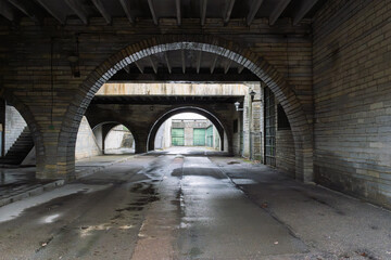 Fototapeta premium Brick Arched Tunnel Passageway Outside Abandoned City Hall Building with Wet Pavement. Urban Architecture Featuring Multiple Arches, Symmetrical Perspective and Industrial Design Elements