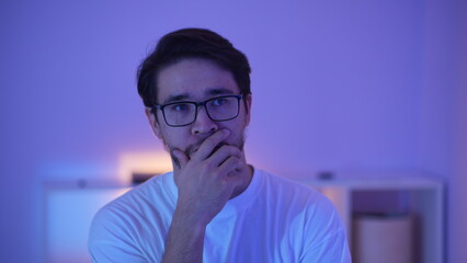 Moody cinematic portrait of a serious bearded man thinking in blue and purple artificial lighting.