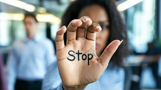 Protective stance: a woman in office with her arm outstretched holding says stop, symbolizing resistance, boundaries, and awareness, addressing the concept of harassment at work with determination.