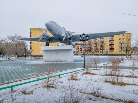 Soviet Lisunov Li-2 aircraft monument towers in Baikonur residential area, Kazakhstan, surrounded by Soviet-era apartments.
