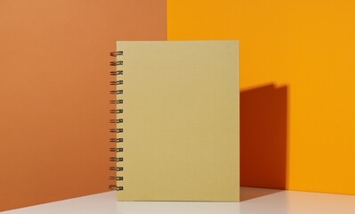 A yellow spiral notebook on a white table against a vibrant orange and yellow background