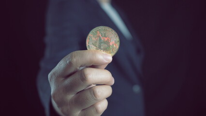 Close up of a person holding a golden bitcoin coin with a red and green trading graph overlay representing cryptocurrency market volatility and digital asset investment trends