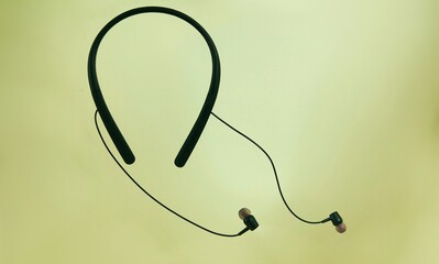 Neckband headphones with earbuds against a gradient green background