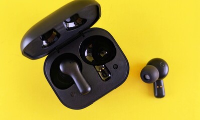 Wireless earbuds in a black charging case on a vibrant yellow background viewed from above