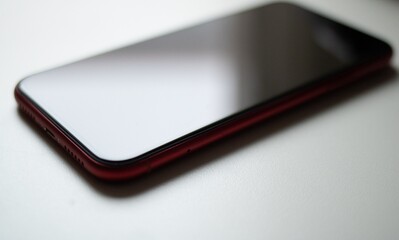 A smartphone with a black screen lies on a white surface viewed from a high angle