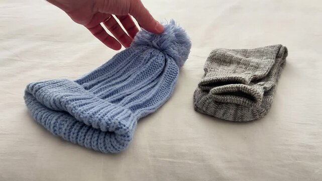 A blue knitted beanie with pom-pom and folded gray socks rest on a soft surface, showcasing cozy winter accessories, textured fabric, and a simple seasonal setup