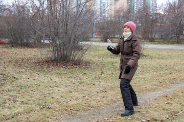 Naklejka premium Elderly woman in winter clothes playing badminton in an autumn park. Active senior lifestyle, outdoor recreation for healthy living.