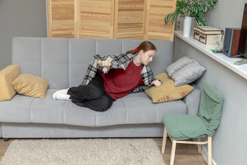 A young woman adjusts her pillow and lies down to rest on the sofa in her room. Free time and relaxation at home. A cozy living space.