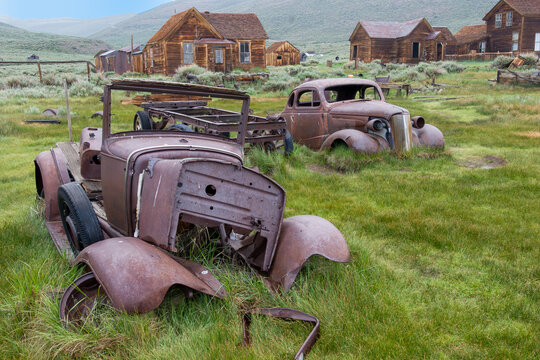 Rusted Cars in the Ghost Town Bodie, a former gold rush town with wooden huts in background