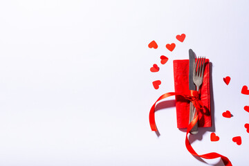Overhead shot of cutlery tied with ribbon on red napkin by hearts on white background, copy space