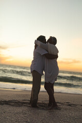 Full length side view of happy senior couple embracing each other while standing at beach