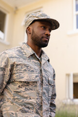 Naklejka premium African american army man wearing camouflage uniform and cap looking away against house