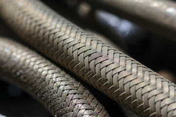 Close up view of old braided metal hose pipe with industrial texture showing metallic curve...