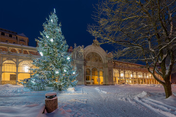 A beautifully decorated Christmas tree glowing in front of the historic colonnade in a snowy winter early morning. A festive holiday atmosphere in a famous spa town Marianske Lazne (Marienbad)