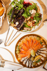 Top view of festive dinner table featuring sliced salmon, herring appetizer and fresh green salad.
