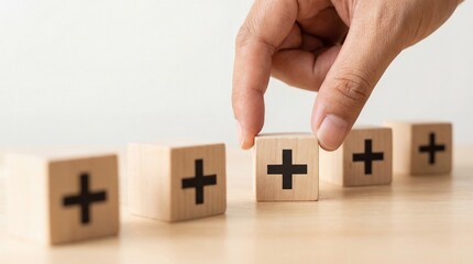 A hand places a wooden block with a black plus sign into a row of similar blocks on a bright wooden table against a white background under soft lighting symbolizing addit