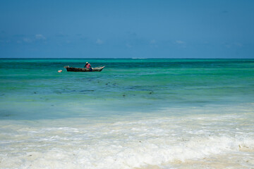 A lonely wooden fishing boat floating on the vibrant turquoise waters of the Indian Ocean near the white sandy shores of Zanzibar.