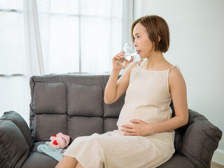 Asian pregnant woman drinking water for the health of herself and her unborn baby.