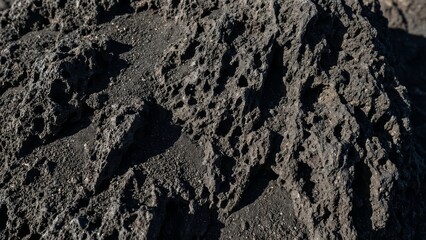 Close-up of rugged, dark volcanic rock with intricate textures and deep shadows under natural light.
