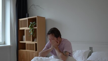 Healthy morning of young man waking up in cozy bed stretching arms and neck, rubbing eyes trying to perk up after night sleep for start day. Well rested male awaked in bedroom looking window. 