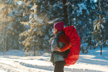 a female tourist with a red backpack walks through a winter snow-covered coniferous forest