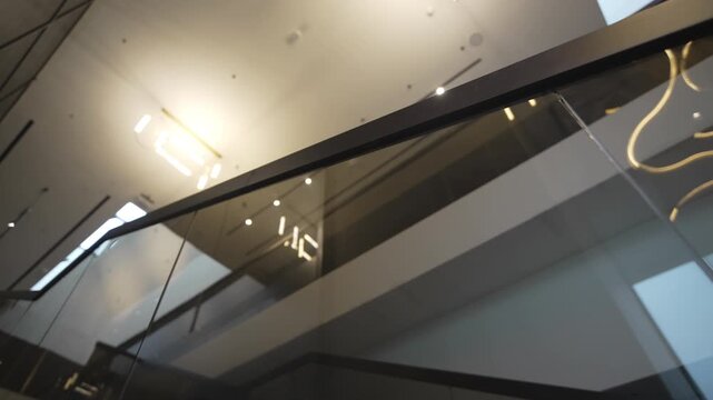Tinted glass railings reflect ceiling chandeliers creating elegant visual rhythm. Smooth surfaces amplify light depth and modern atmosphere