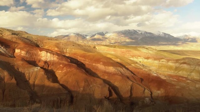 Vibrant Red Layered Hills With Striations, Sunlit Sandstone Outcrops And Painterly Bands Of Ochre And Rust, Deep Shadowed Gullies, Distant Snowy Peaks On Horizon, Dramatic Geological Texture, Warm