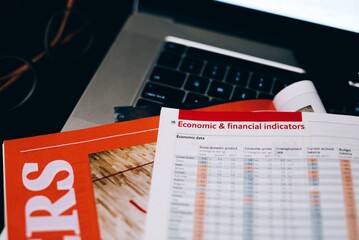 Economic And Financial Indicators Page On Desk With Laptop And Magazine Data And Charts