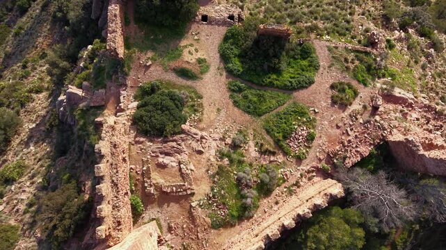Aerial view of ancient castle ruins near Serra village, gently rising to reveal rocky terrain and pine forests across the Sierra Calderona Natural Park in the Valencia region of Spain
