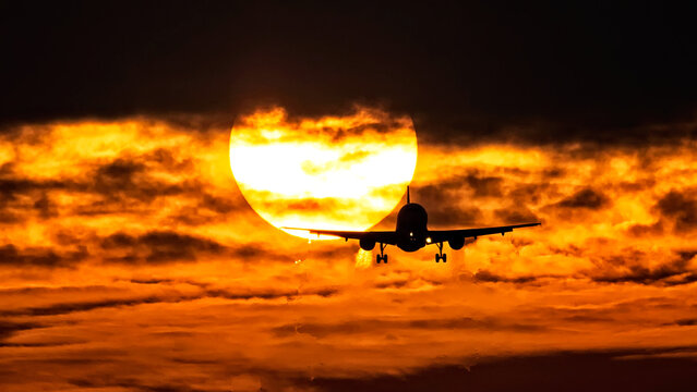 View of a silhouette of an airplane gracefully descends against a fiery sunset backdrop, casting an ethereal glow across the sky, Schiphol, Noord-Holland, Netherlands.