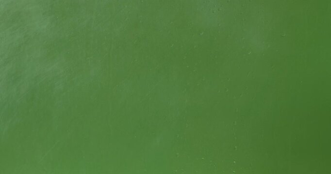 Close up of sprayed liquid and wet glass with water droplets and rain streaks on a bright green chroma key background, ideal for visual effects and background replacement. Slow motion.
