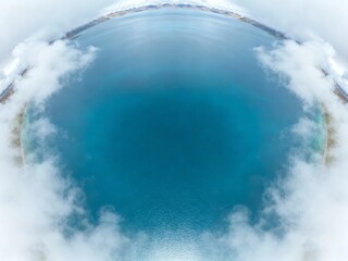 Aerial view of a circular blue lagoon surrounded by clouds and landmass